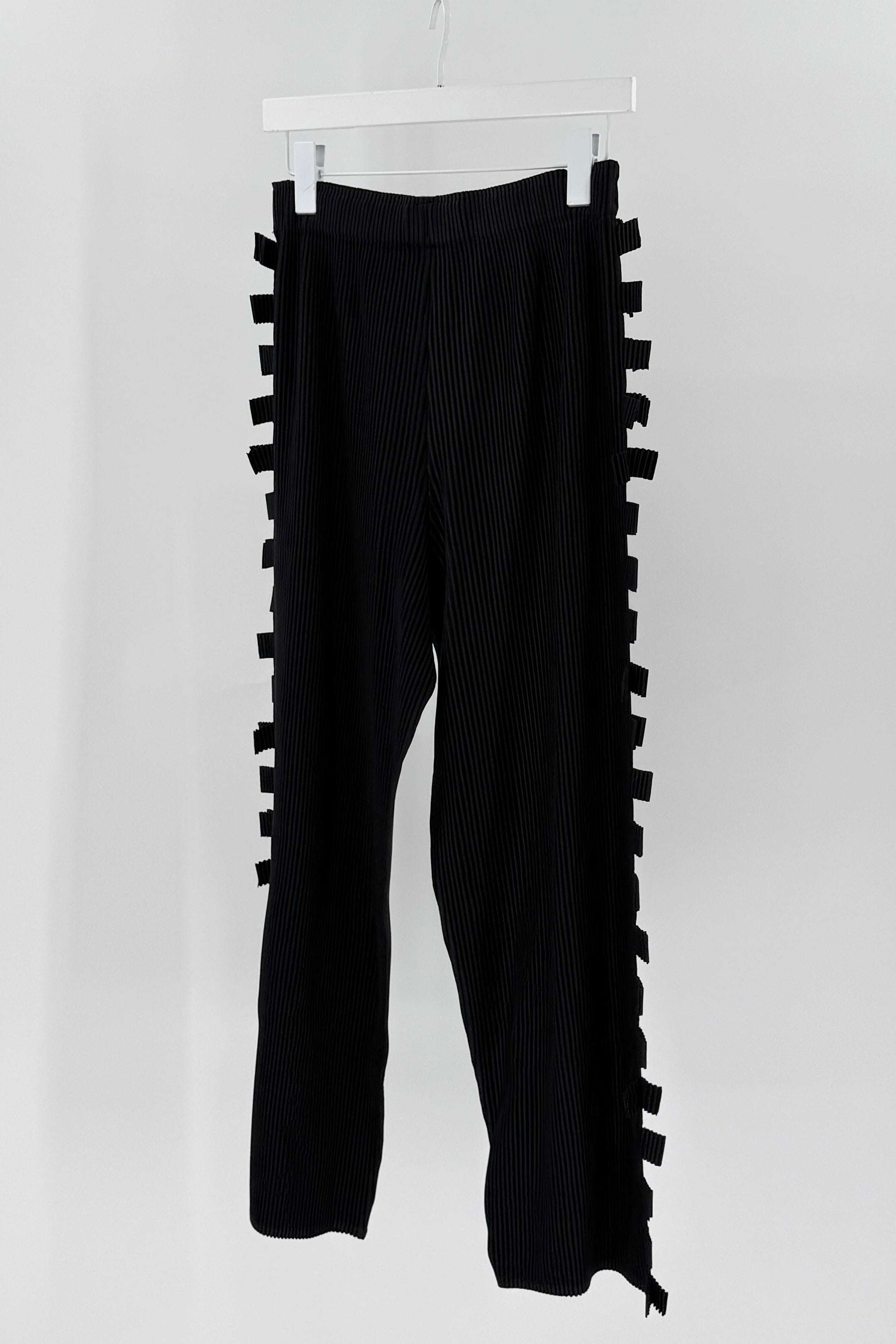 Black pants with ruffled side panels on a white hanger against a white background