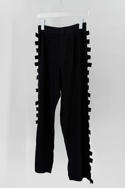 Black pants with ruffled side panels on a white hanger against a white background