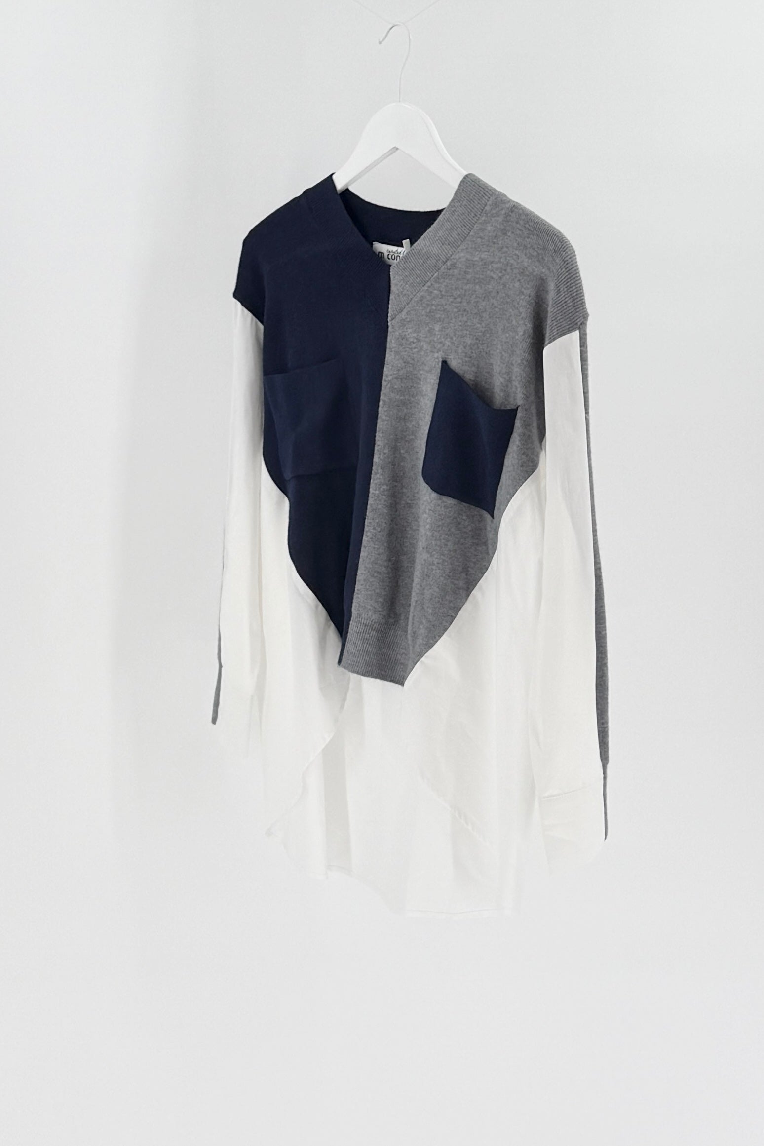 Color-blocked sweater with navy, gray, and white sections on a hanger against a white background