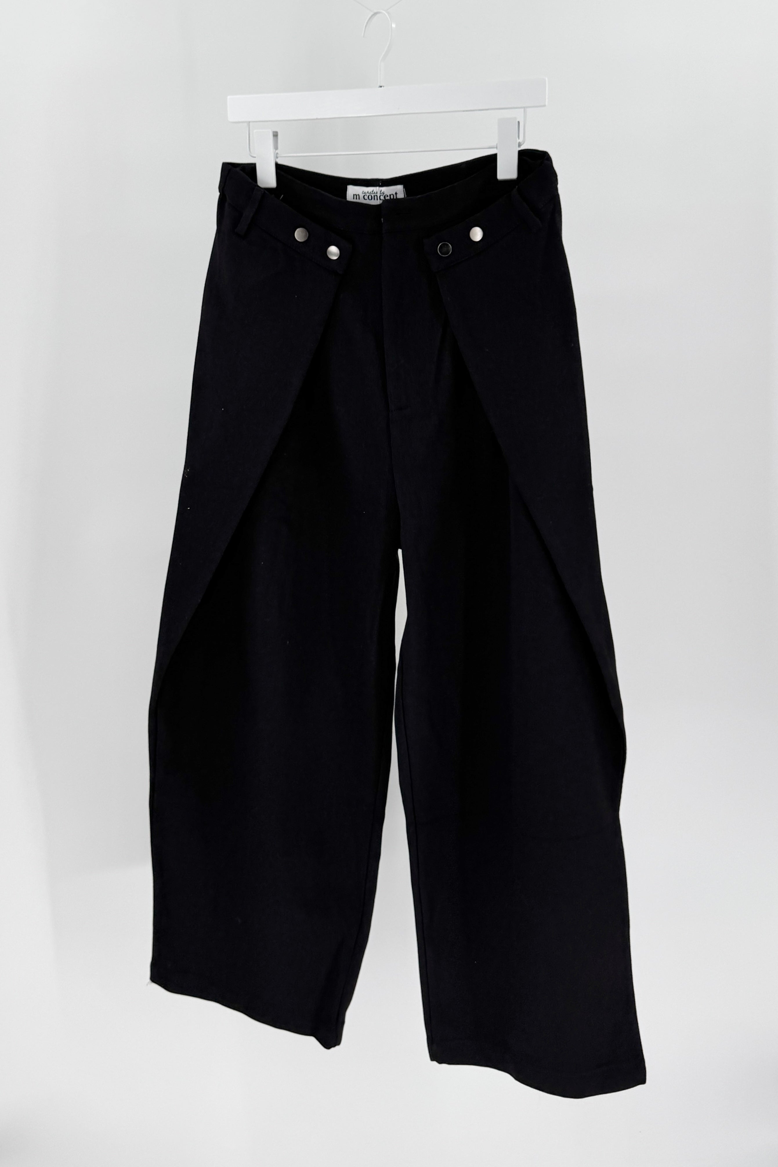 Black pants hanging on a white rack against a white background