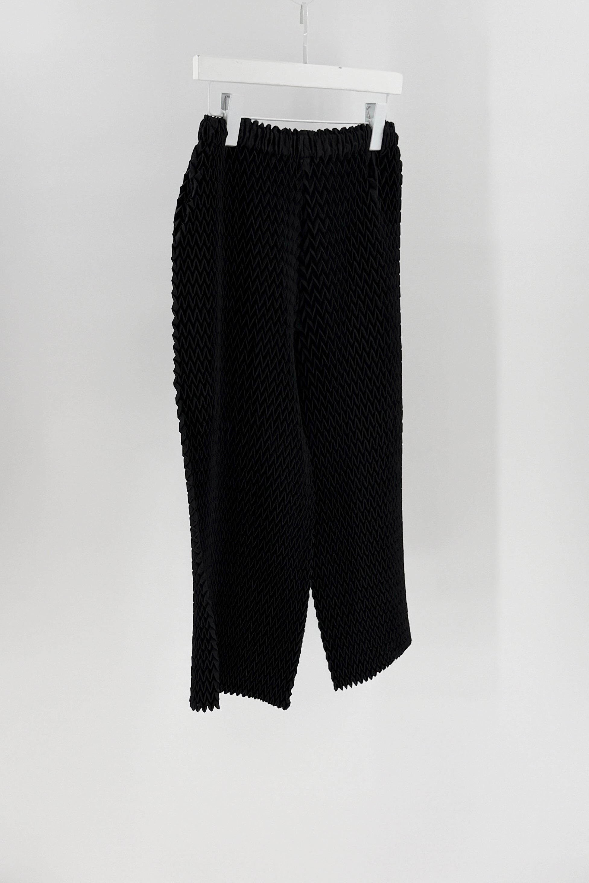Black textured pants hanging on a white rack against a white background