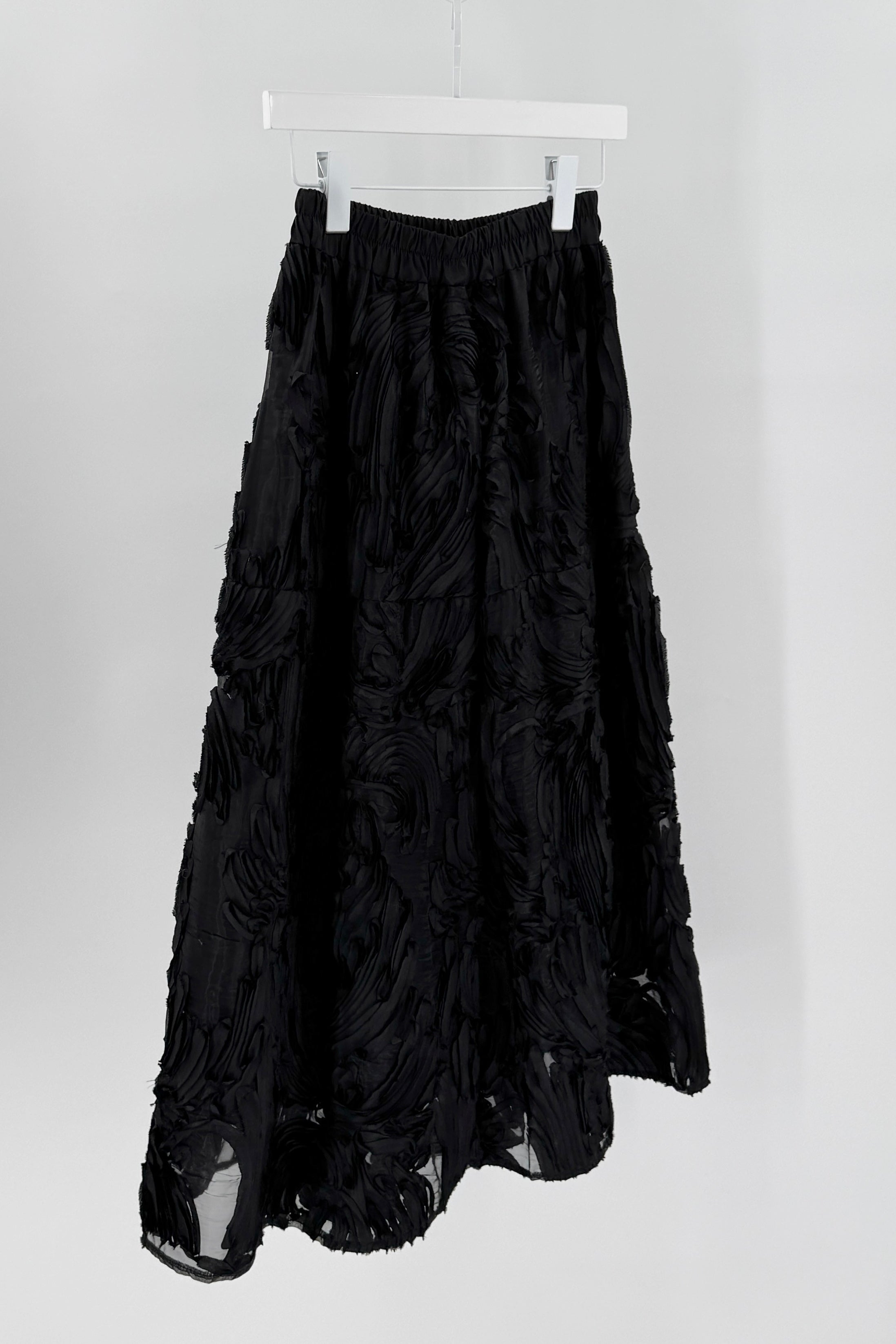 Black ruffled skirt on a white hanger against a light gray background