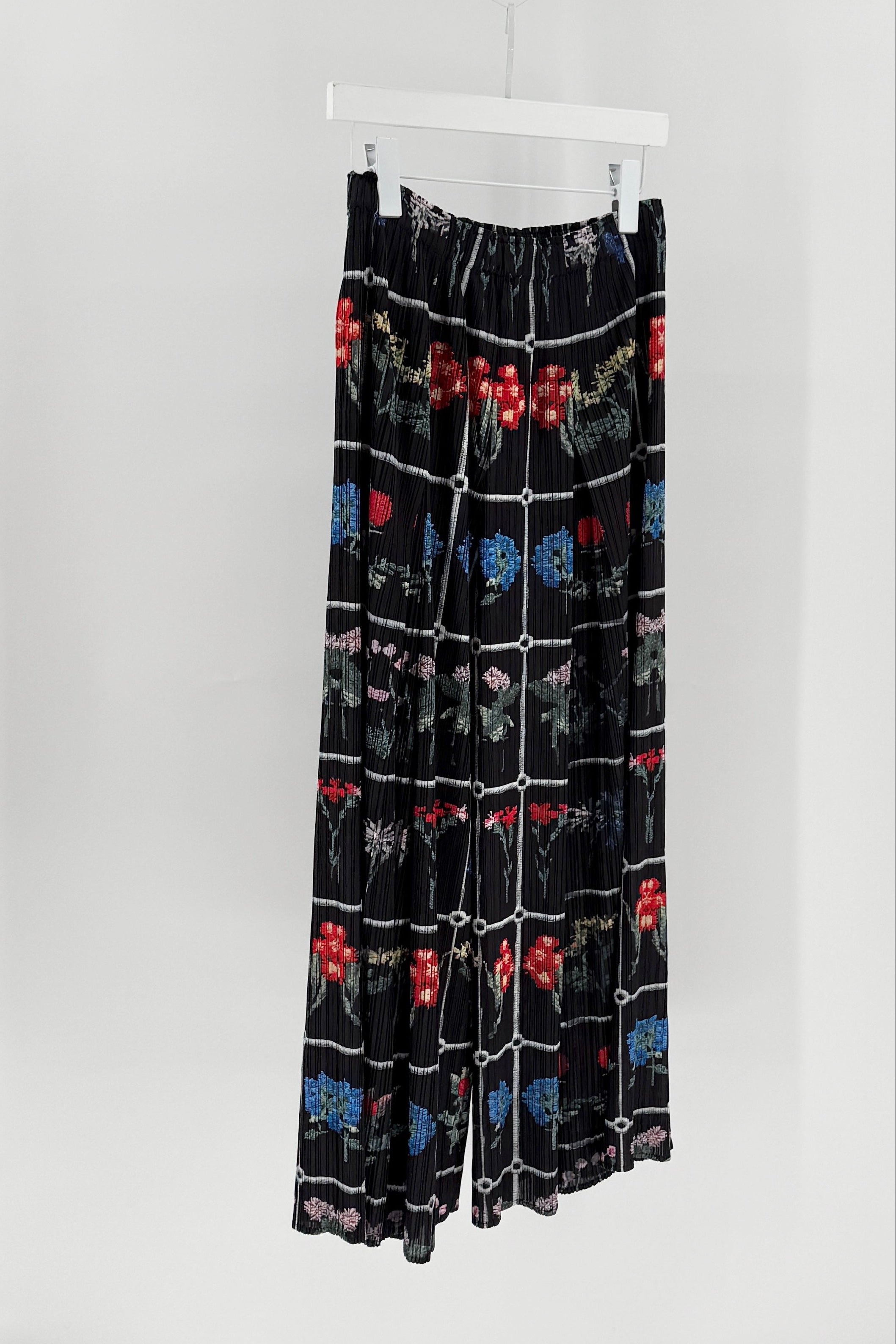 Black pants with colorful pattern hanging on a white rack against a white background