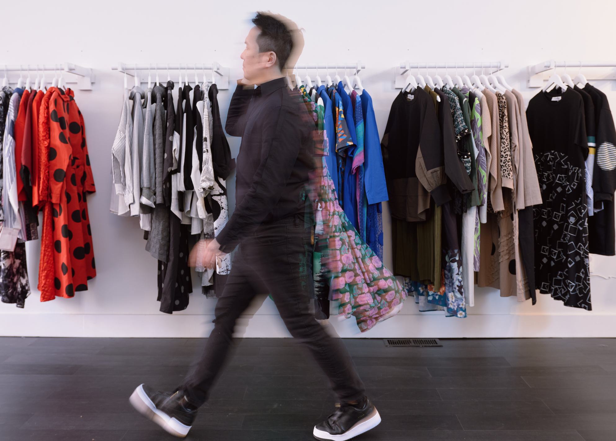 Man walking past a clothing rack with various garments in a store setting.