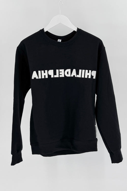 Black sweatshirt with 'PHILADELPHIA' embroidered in a mirror design on it on it, hanging against a white background